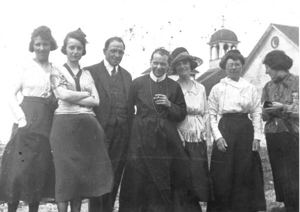 173: Julia McCarthy (with the 'Y-neck' top) and her sister Kit McCarthy (later to be Sr. Chrysostom,  right of the priest, with large hat), at Argentia, with Holy Rosary Church in the background.  (circa 1920)  - daughters of Denis McCarthy &amp;amp; Sarah Withers